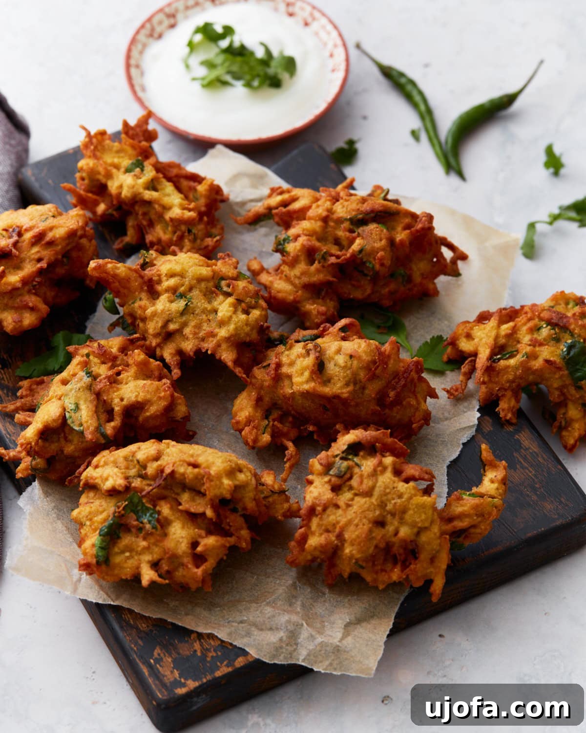 Savory Golden Crisps 2 Golden-brown pakoras arranged on parchment paper over a dark wooden board, served with a bowl of creamy white dipping sauce and fresh herbs.