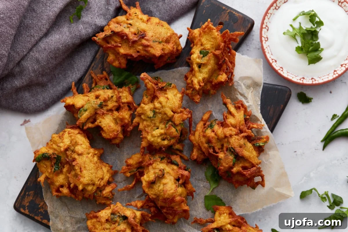Savory Golden Crisps 10 A styled shot of crispy pakoras served on parchment paper with a side of creamy dipping sauce and fresh green chili peppers scattered around.