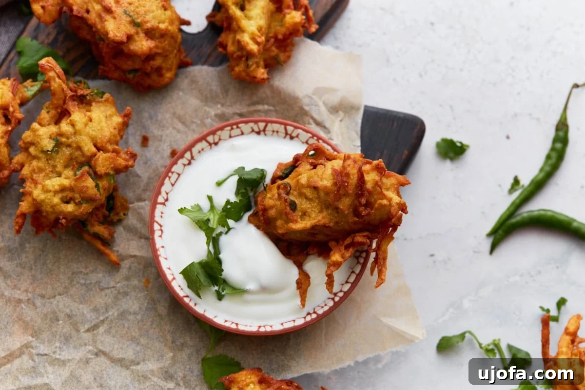 Savory Golden Crisps 11 A single pakora dipped into a small bowl of yogurt sauce, garnished with chopped cilantro for serving.