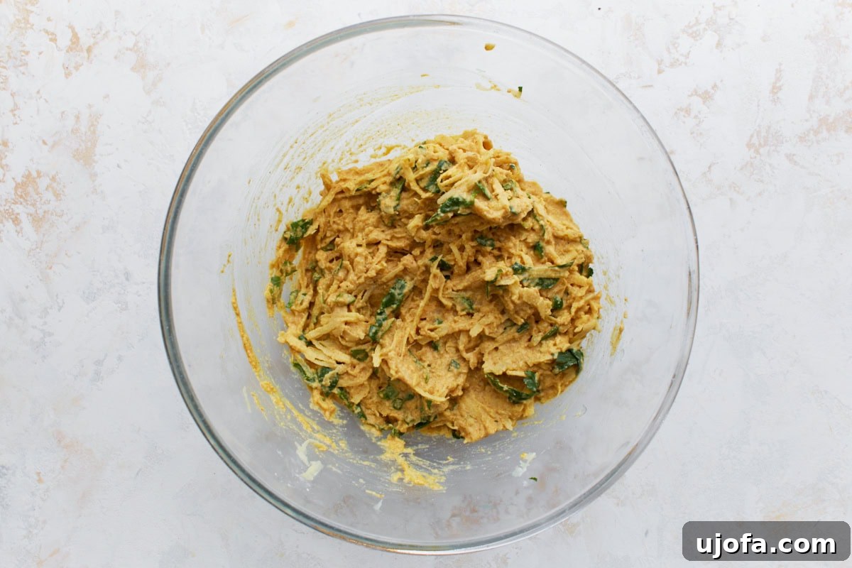 Savory Golden Crisps 7 Pakora batter in a bowl with shredded potatoes, spinach, and cilantro fully mixed into the thick spiced paste.