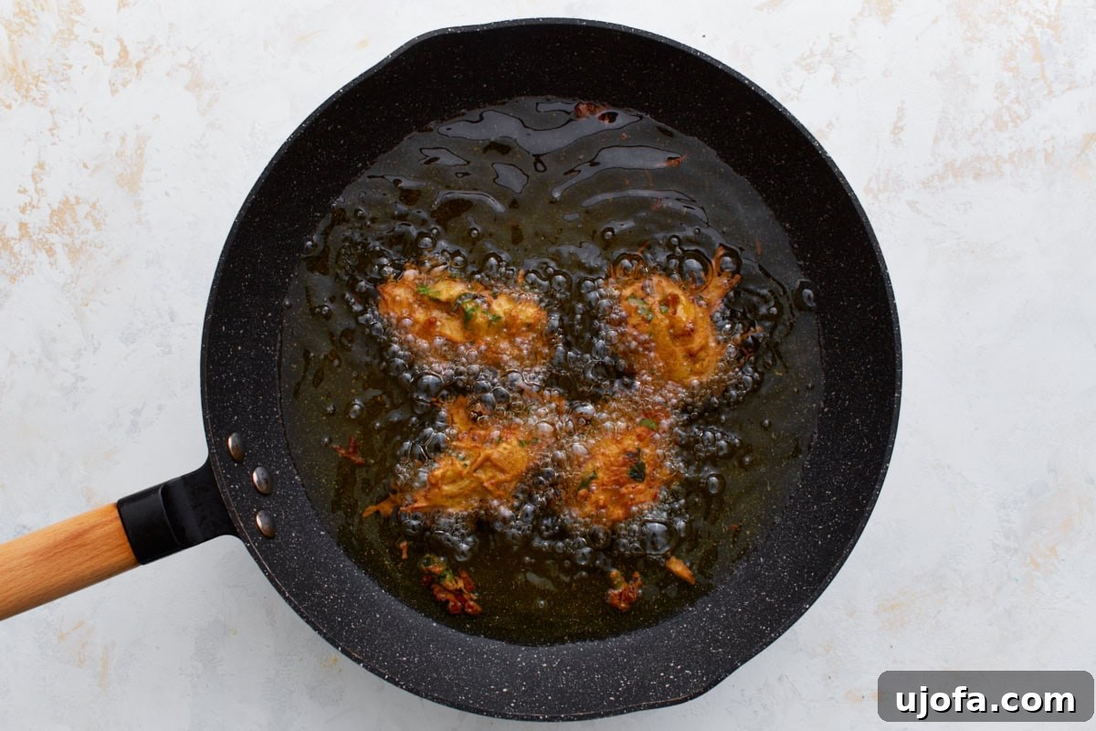 Savory Golden Crisps 8 Several pakoras sizzling in hot oil in a black frying pan, bubbling as they turn golden and crisp.