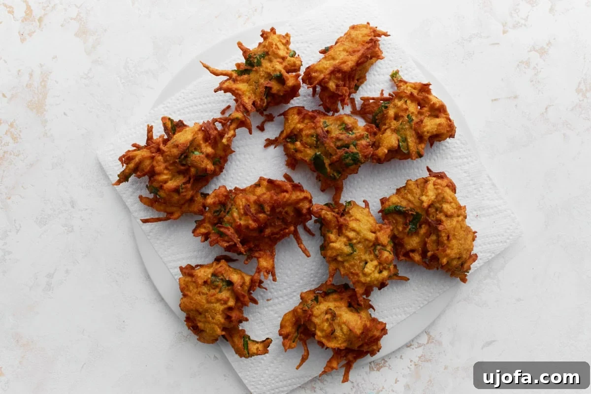 Savory Golden Crisps 9 Freshly fried pakoras cooling on a white paper towel-lined plate, showing their crispy, golden texture.