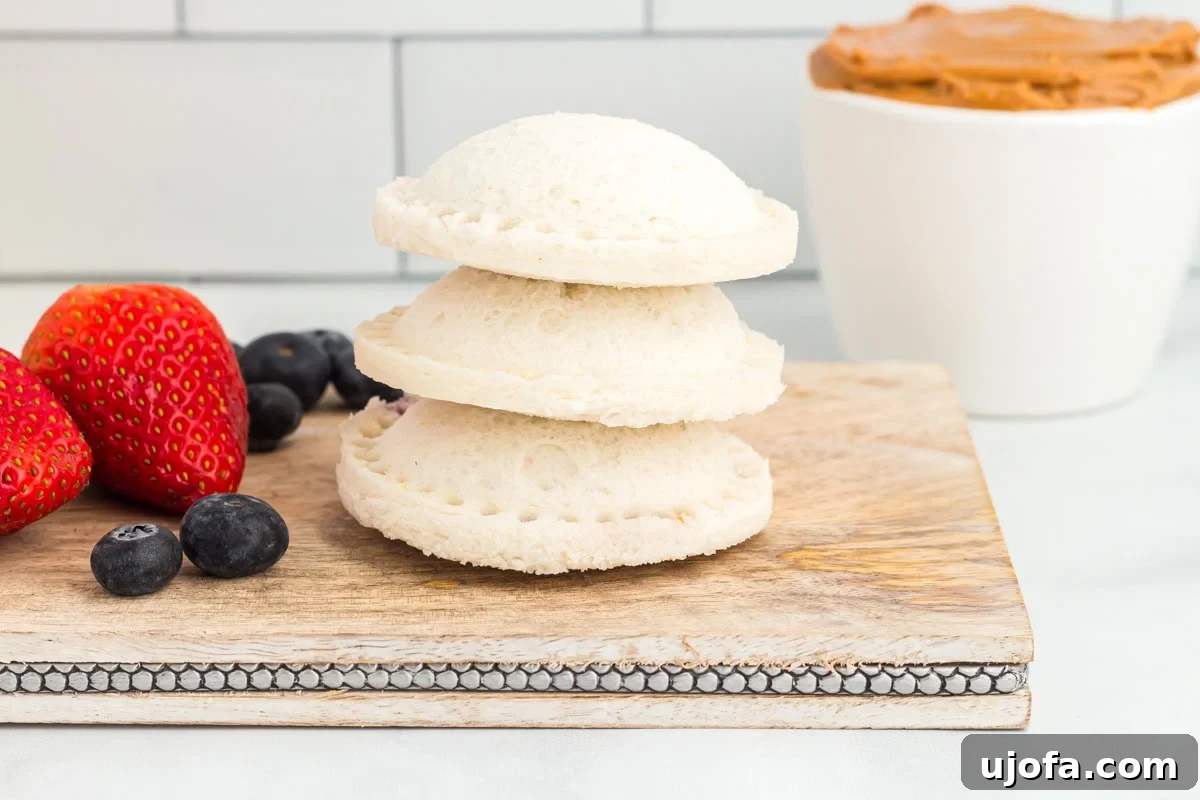 GF Lunchbox Wonders 10 A stack of three homemade gluten-free uncrustables on a rustic wooden board with fresh strawberries and blueberries in the background.
