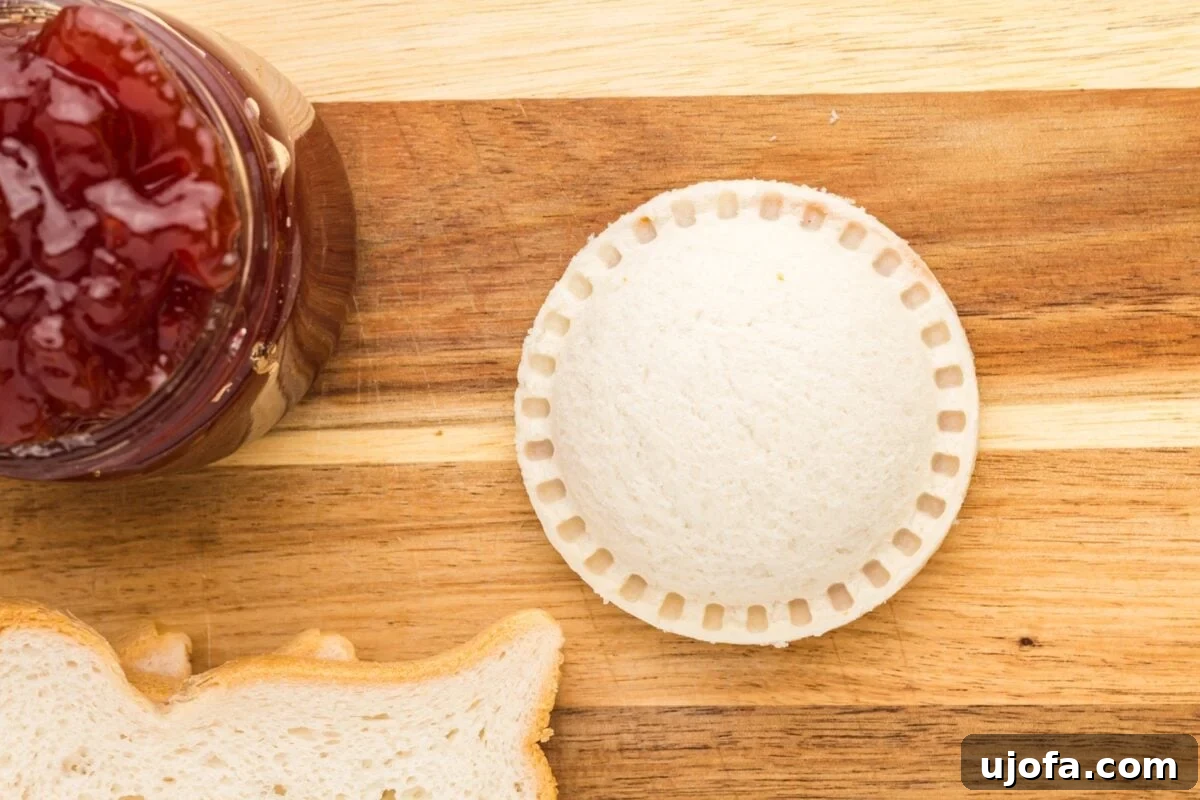 GF Lunchbox Wonders 9 A sealed homemade gluten-free uncrustable next to a jar of strawberry jam and slices of gluten-free bread on a cutting board.