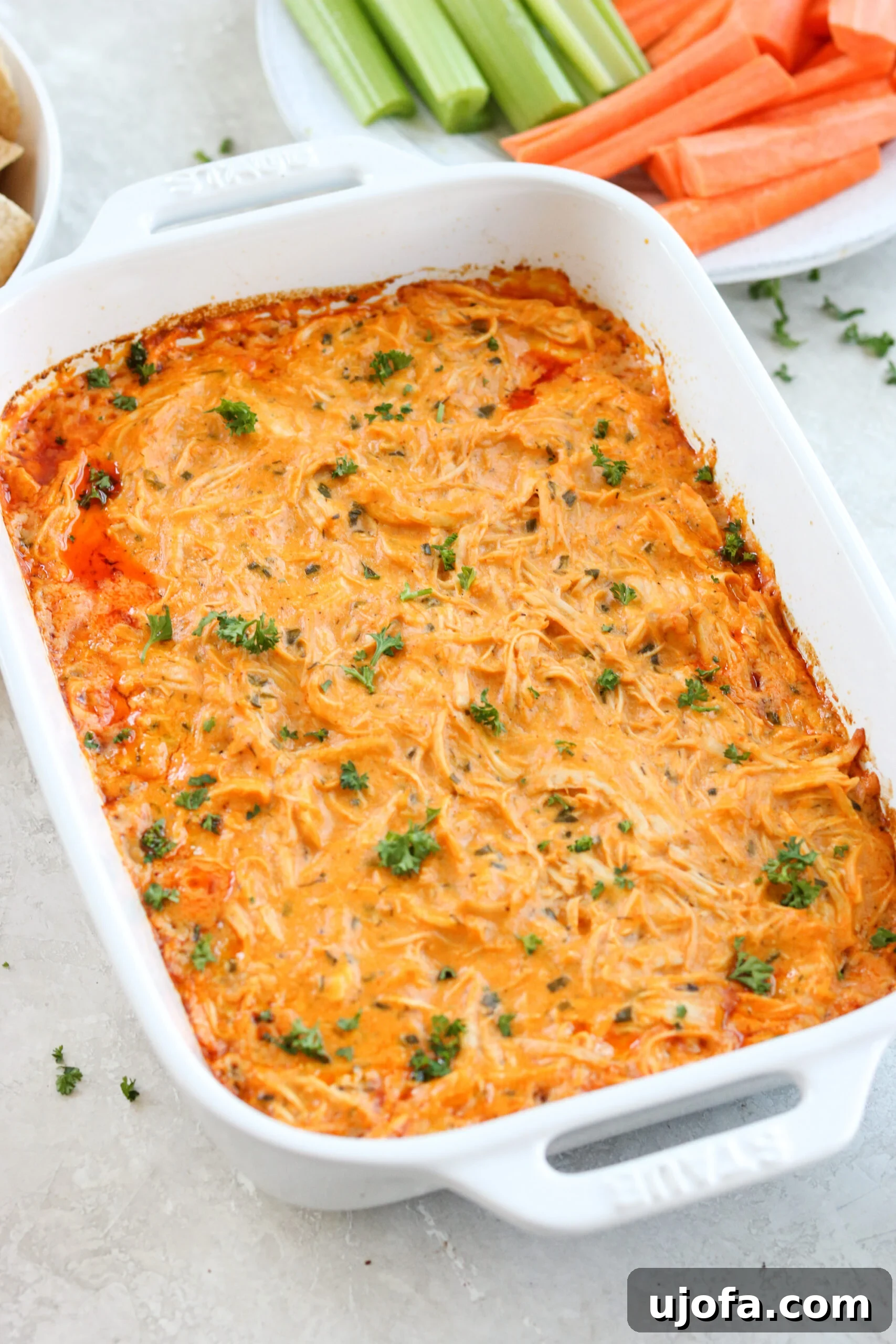 Easy Instant Pot Keto Buffalo Chicken Dip No Dairy 2 Healthy buffalo chicken dip in a white Staub baking dish topped with parsley with carrots and celery in the background