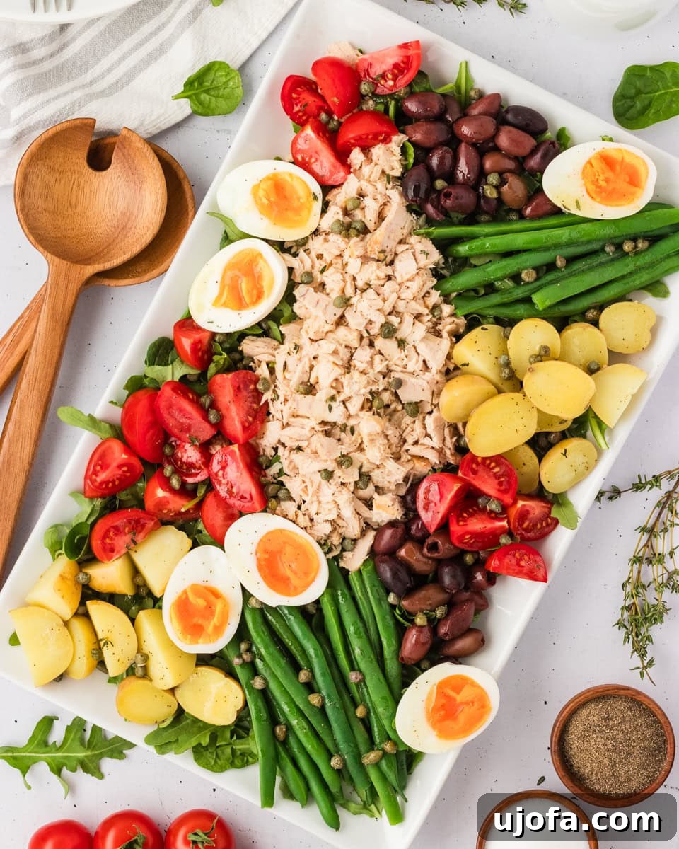 French Riviera Tuna Salad 2 Overhead view of a beautifully arranged Tuna Nicoise Salad on a white rectangular platter with eggs, tomatoes, olives, green beans, potatoes, and tuna.