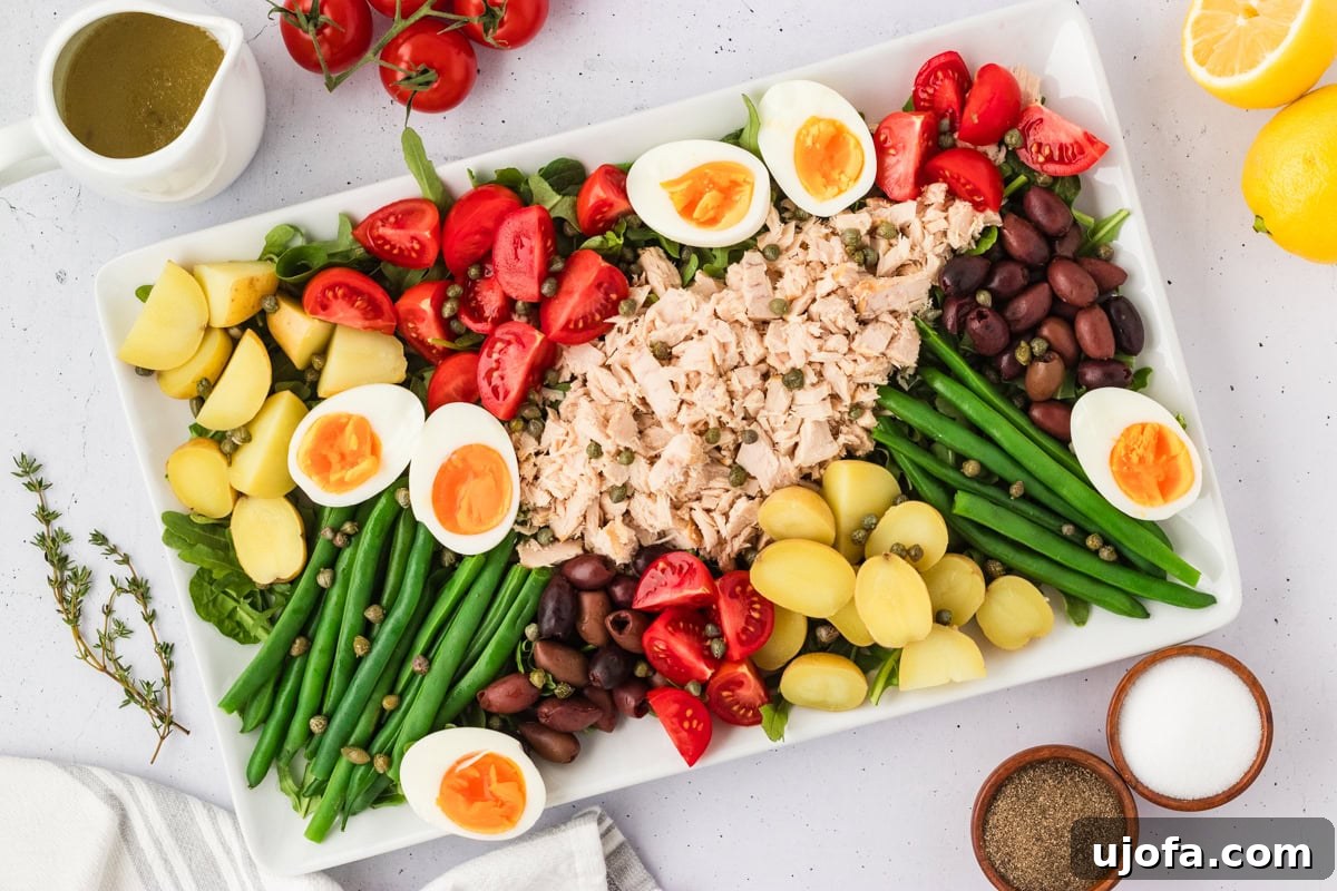 French Riviera Tuna Salad 10 Fully assembled Tuna Nicoise Salad with vinaigrette in a pitcher nearby, tomatoes and lemons in the background.