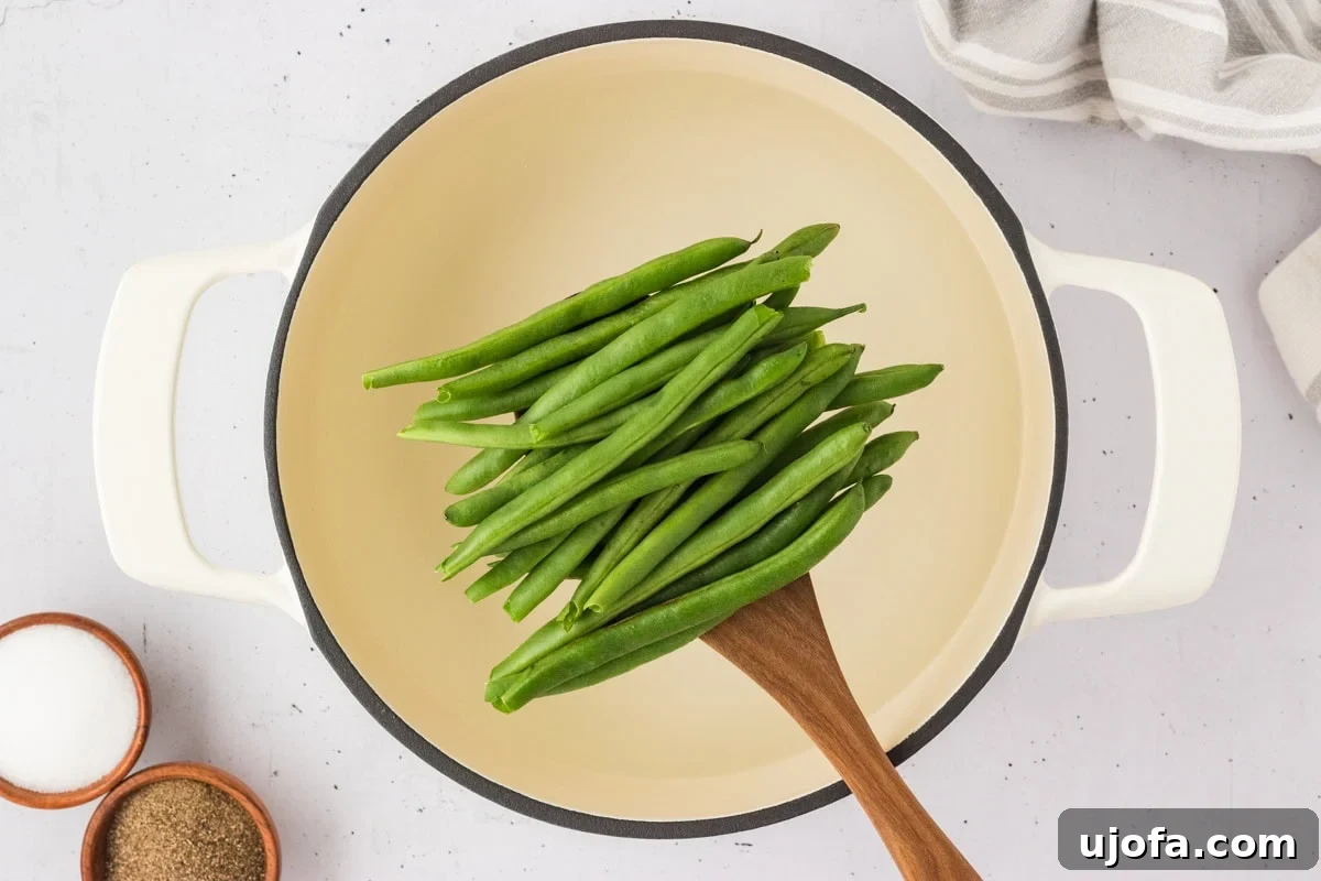 French Riviera Tuna Salad 6 Raw green beans in a cream-colored pot being stirred with a wooden spoon, ready for blanching.