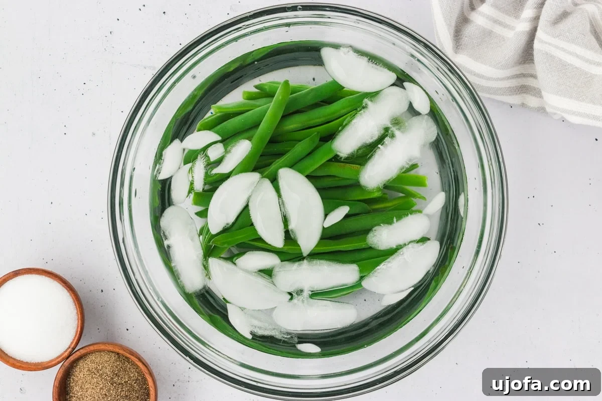 French Riviera Tuna Salad 7 Blanched green beans in a clear bowl filled with ice water to stop cooking, with salt and pepper bowls nearby.