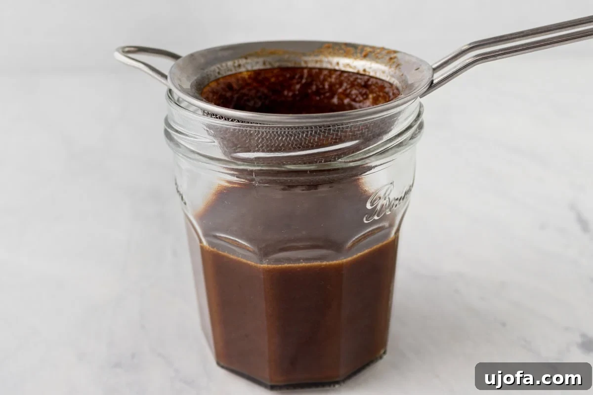 Gluten-Free Worcestershire from Scratch 11 The finished sauce being poured through a fine mesh sieve into a glass jar to remove solids