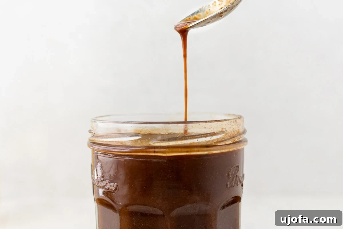 Gluten-Free Worcestershire from Scratch 12 A close-up of a spoon dripping a thin stream of dark Worcestershire sauce back into the jar below.