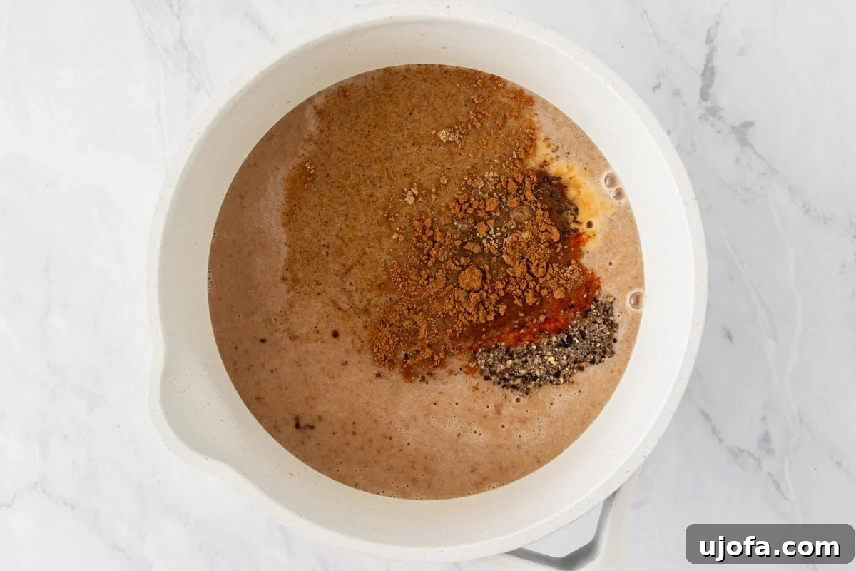 Gluten-Free Worcestershire from Scratch 8 A saucepan containing the blended mixture with various spices like black pepper, cinnamon, and mustard powder freshly added on top.