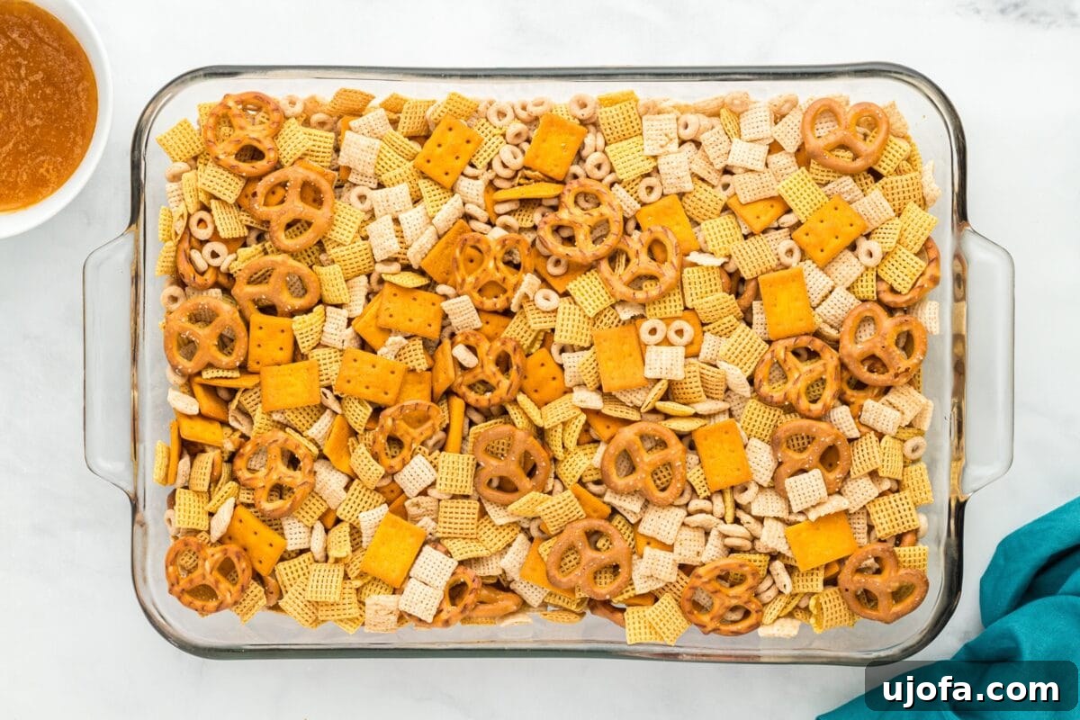 Savory Gluten-Free Party Mix 4 Glass baking dish filled with an unbaked mix of gluten-free cereals, pretzels, and crackers, with a bowl of sauce nearby.