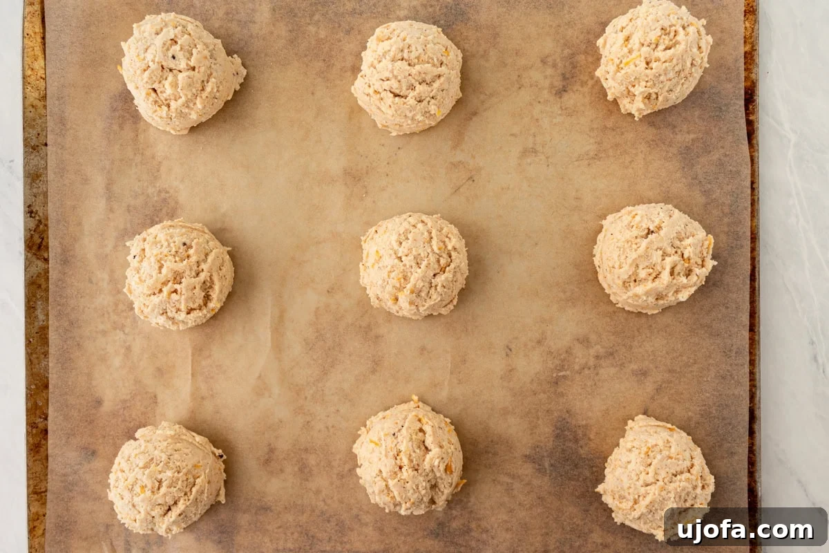 Fluffy Gluten-Free Drop Biscuits 9 A neatly arranged baking sheet displaying nine perfectly scooped portions of biscuit dough, evenly spaced on parchment paper, ready for baking.