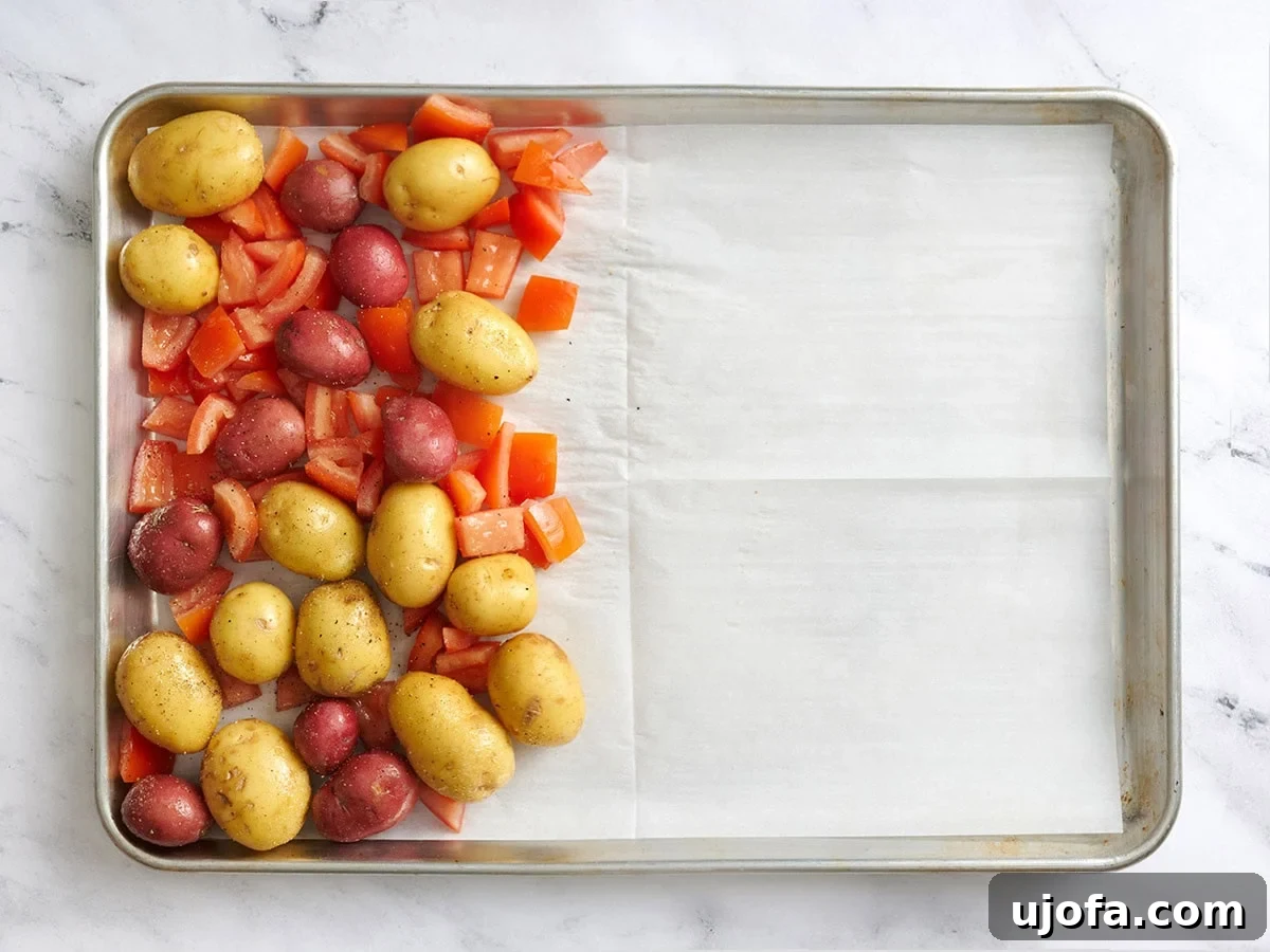 Tangy Tzatziki Black Bean Power Bowl 5 Seasoned new potatoes and diced tomatoes on 1/3 of a parchment lined baking sheet, ready for roasting.