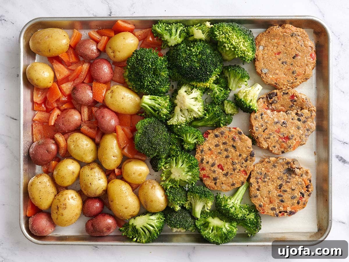 Tangy Tzatziki Black Bean Power Bowl 7 Overhead view of new potatoes and diced tomatoes on 1/3 of a parchment lined baking sheet, fresh broccoli florets down the center of the baking sheet, and 4 black bean burgers on the remaining 1/3, ready for further roasting.
