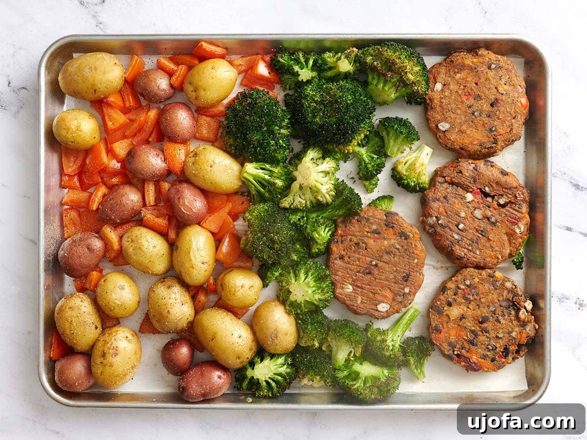 Tangy Tzatziki Black Bean Power Bowl 9 Overhead view of fully roasted new potatoes, diced tomatoes, broccoli florets, and black bean burgers on a parchment lined baking sheet, after baking.