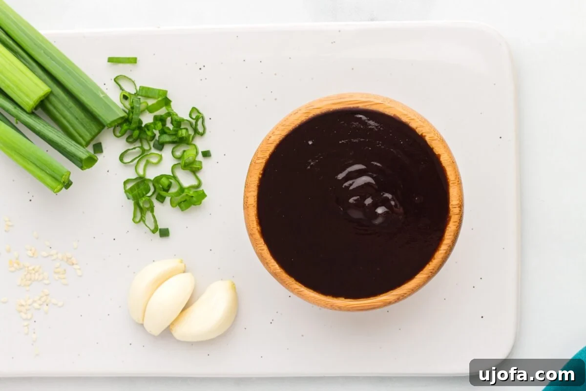 Craft Your Own Gluten-Free Hoisin Sauce 7 Bowl of homemade hoisin sauce on a white platter with sliced green onions, garlic cloves, and sesame seeds.
