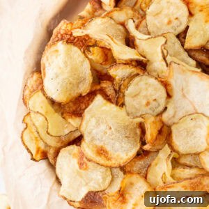 Close-up of a pile of crispy, golden-brown homemade gluten-free potato chips on parchment paper.