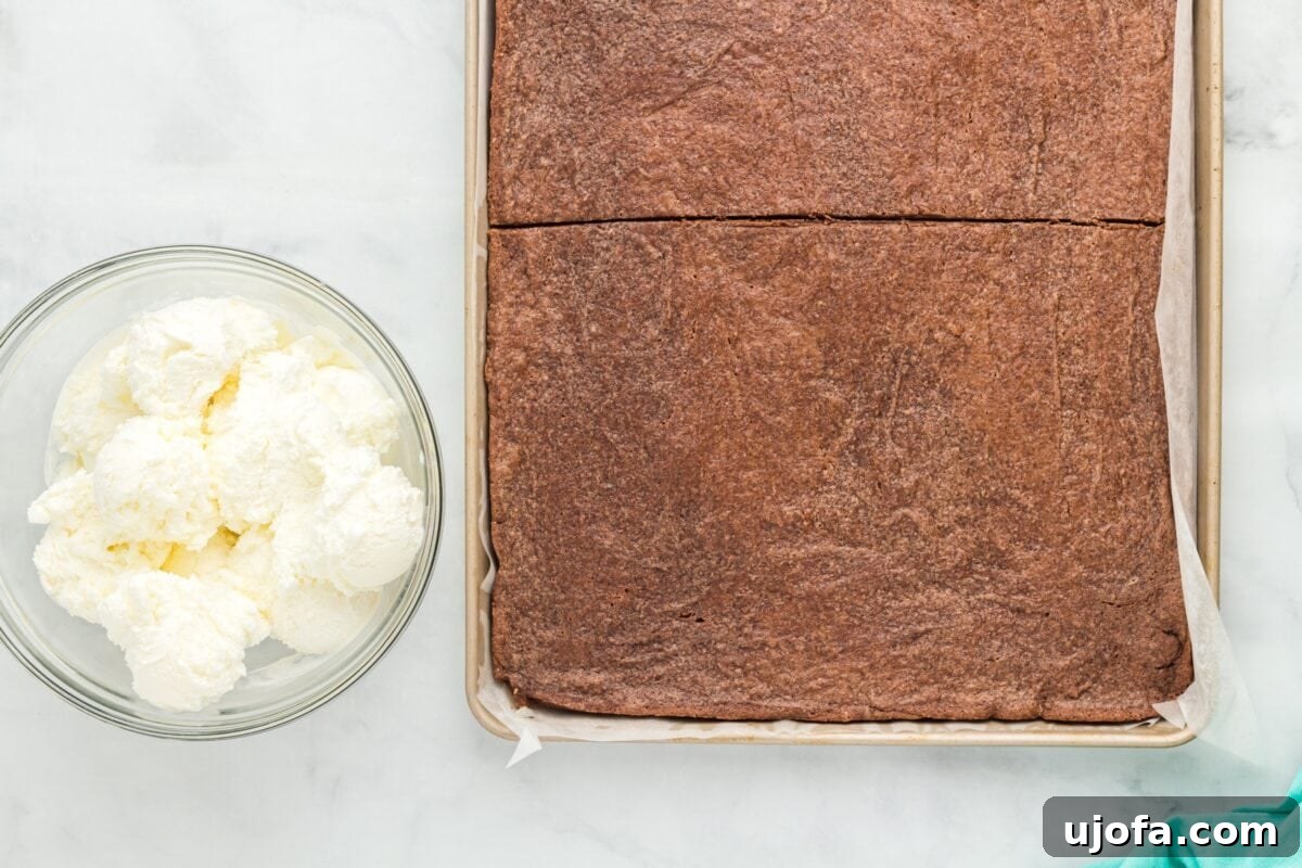 The chilled cookie base has been cut in half on the parchment-lined baking sheet, with a bowl of softened vanilla ice cream ready for layering beside it.