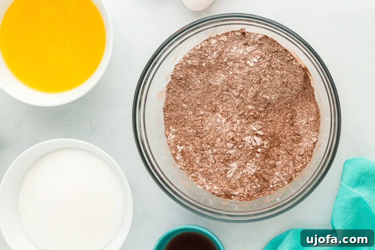 Overhead view of separate bowls for baking: one contains melted butter, sugar, vanilla, and egg, while another holds the dry mixture of cocoa powder and gluten-free flour, ready to be combined.