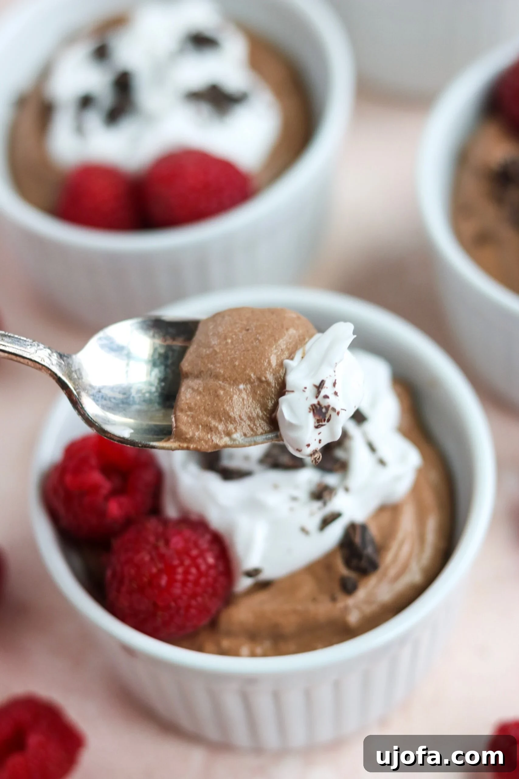 Two servings of Paleo Vegan Chocolate Mousse, one topped with raspberries and chocolate shavings, the other plain, set on a rustic wooden surface.