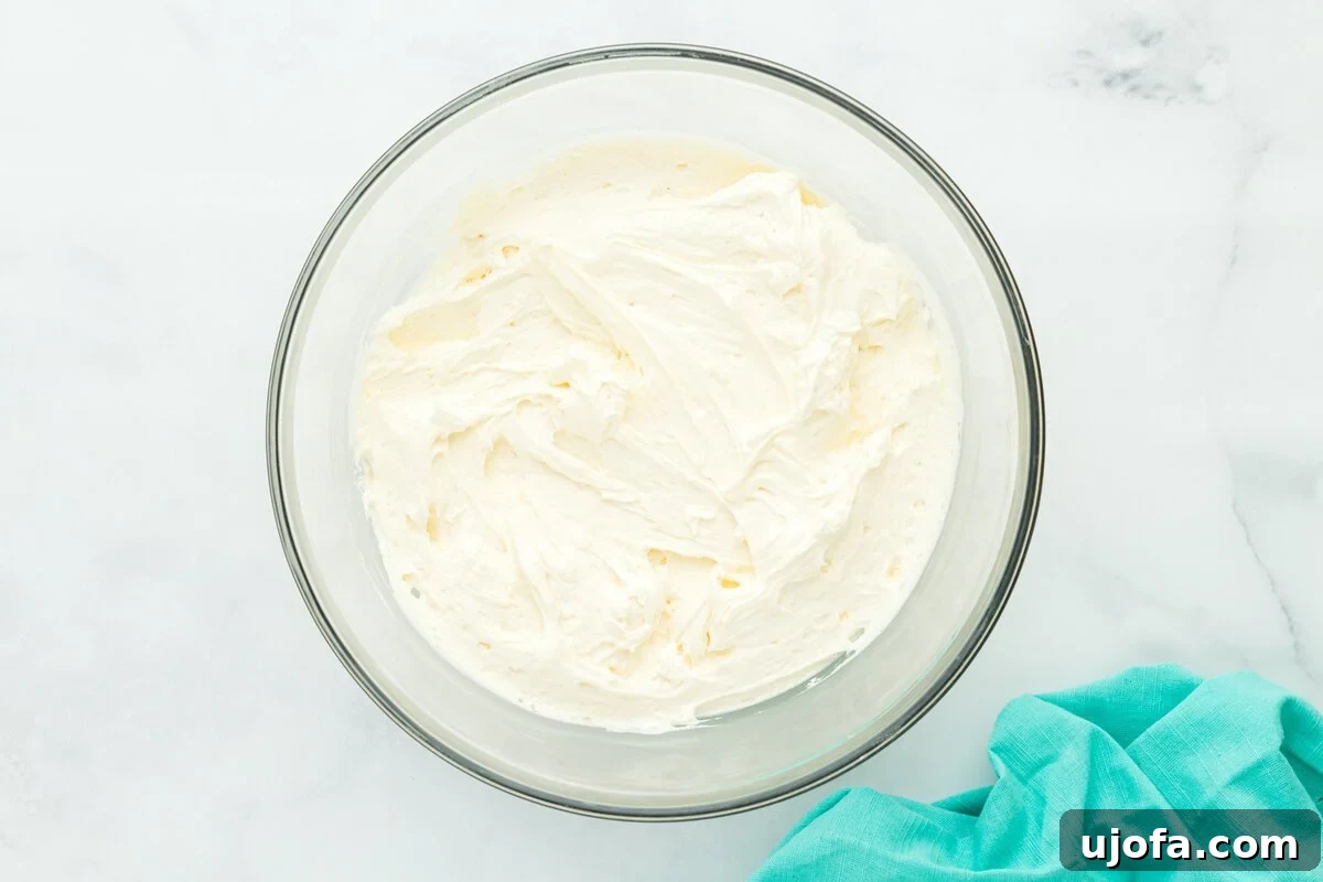 A glass mixing bowl filled with smooth, fluffy vanilla buttercream, ready for frosting the cake.