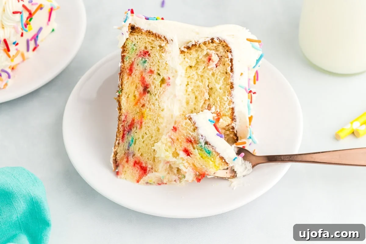 A slice of gluten-free funfetti cake on a white plate with a bite taken out using a copper fork, showing the soft texture and colorful sprinkles inside.