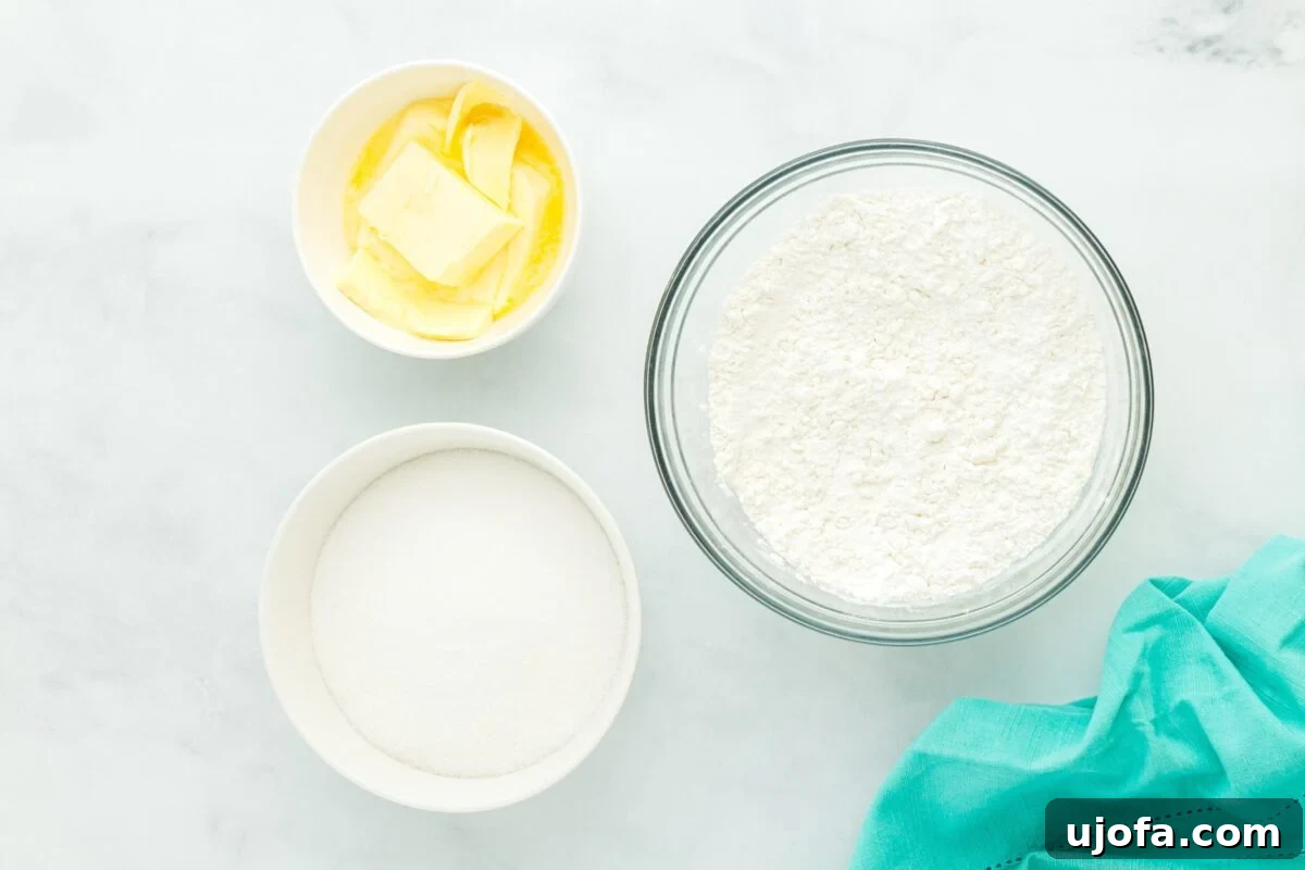 Overhead view of bowls containing butter, granulated sugar, and gluten-free flour on a white surface with a teal cloth.
