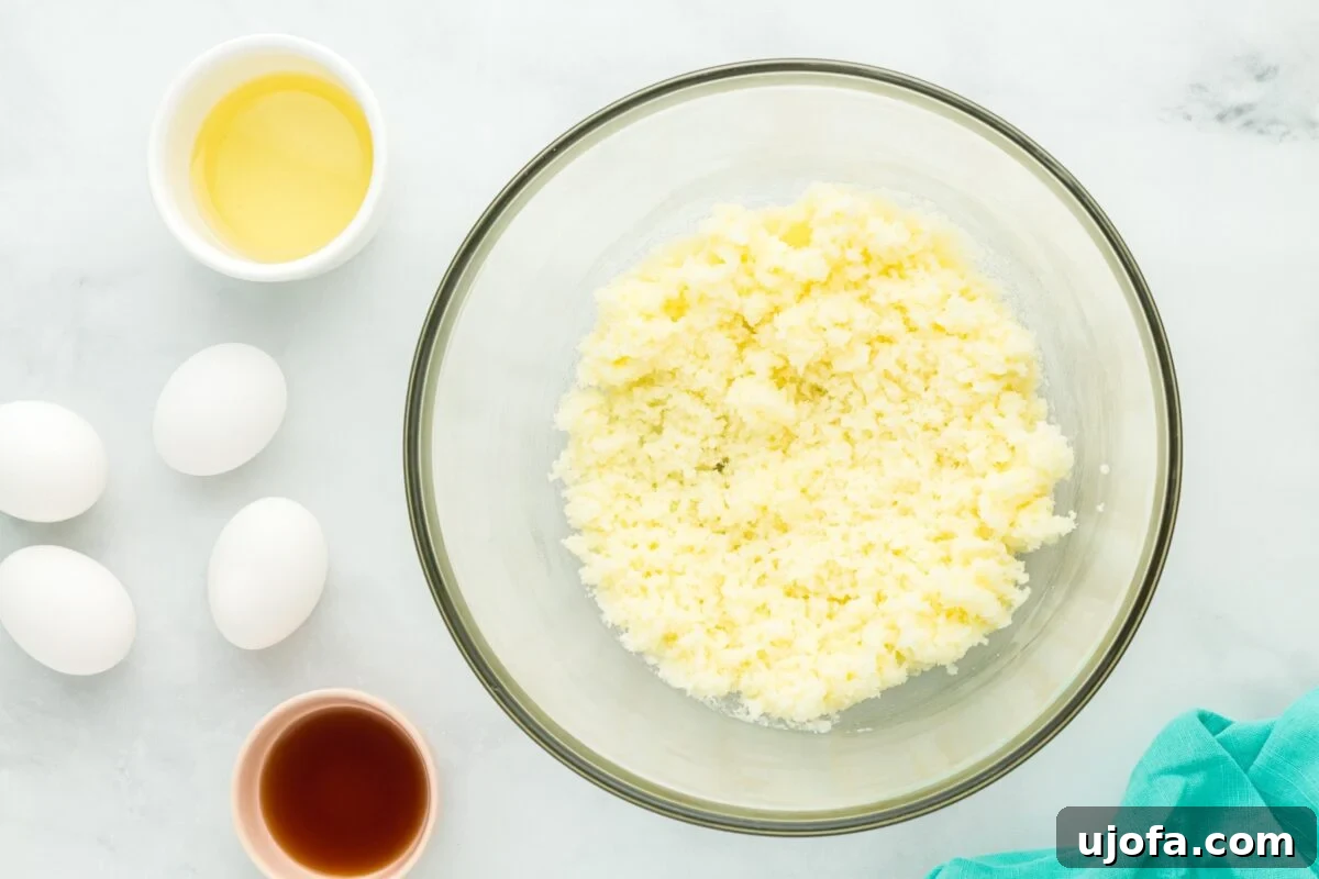 A mixing bowl with creamed butter and sugar surrounded by eggs, vanilla extract, and oil, ready to be combined.
