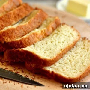 Loaf of homemade gluten-free bread made in a bread machine on a cutting board with a knife and butter in the background