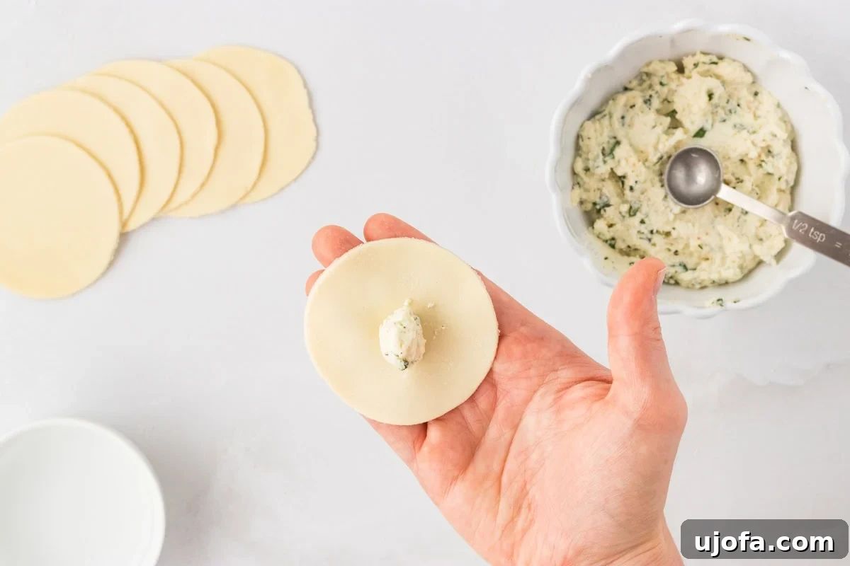 Hand holding a pasta round with a small spoonful of ricotta filling in the center, with more cut rounds and filling in the background