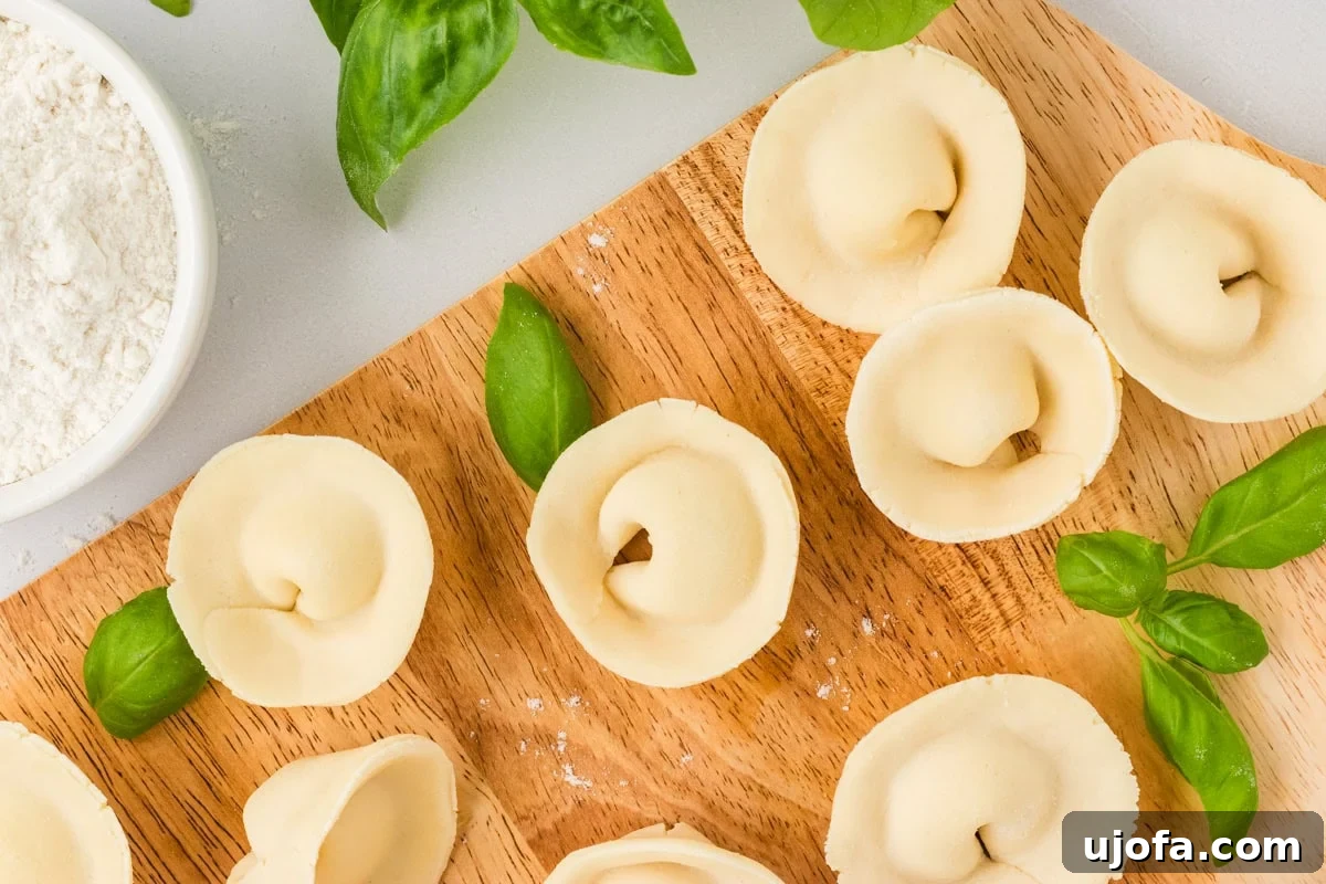 Close-up of raw gluten-free tortellini arranged on a wooden board with fresh basil and a bowl of flour