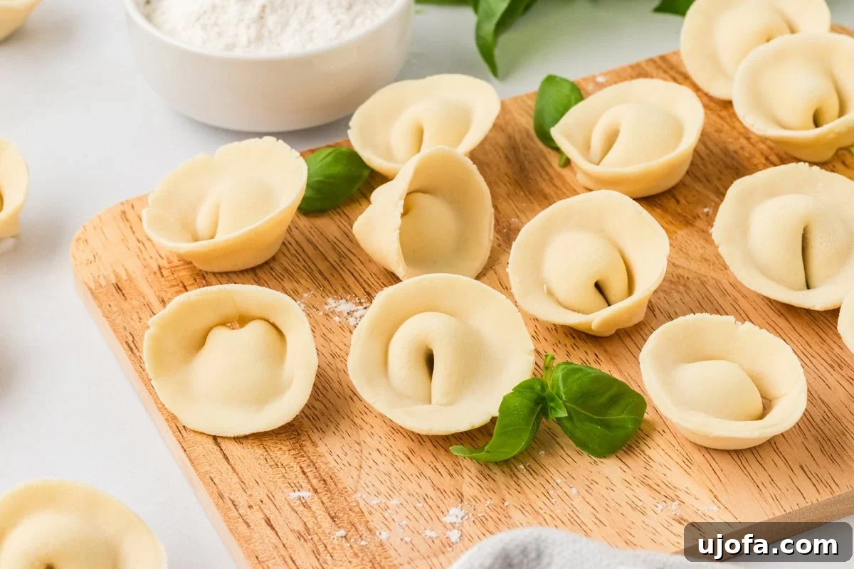 Wooden board topped with gluten-free tortellini and garnished with fresh basil leaves, flour bowl in background