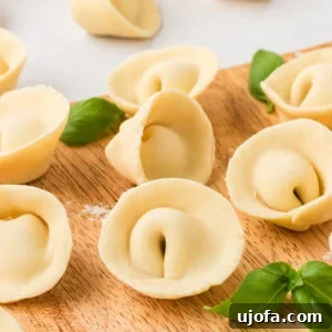 Freshly shaped gluten-free tortellini arranged on a wooden board with fresh basil leaves