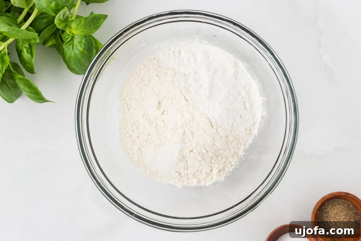 Glass bowl filled with gluten-free flour mixture, surrounded by fresh basil and small wooden bowls of salt and pepper