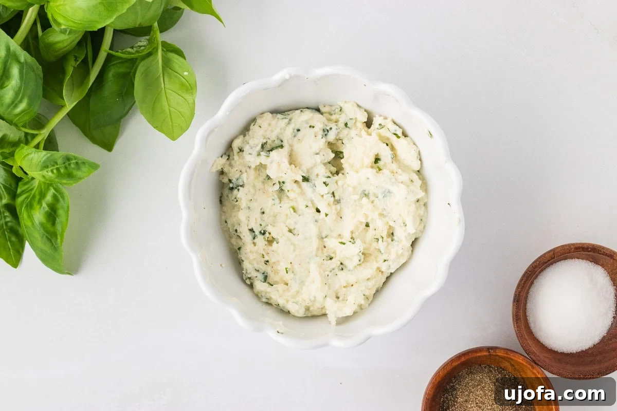 Ricotta, parmesan, and basil filling mixed together in a white bowl, with fresh basil and seasoning bowls nearby