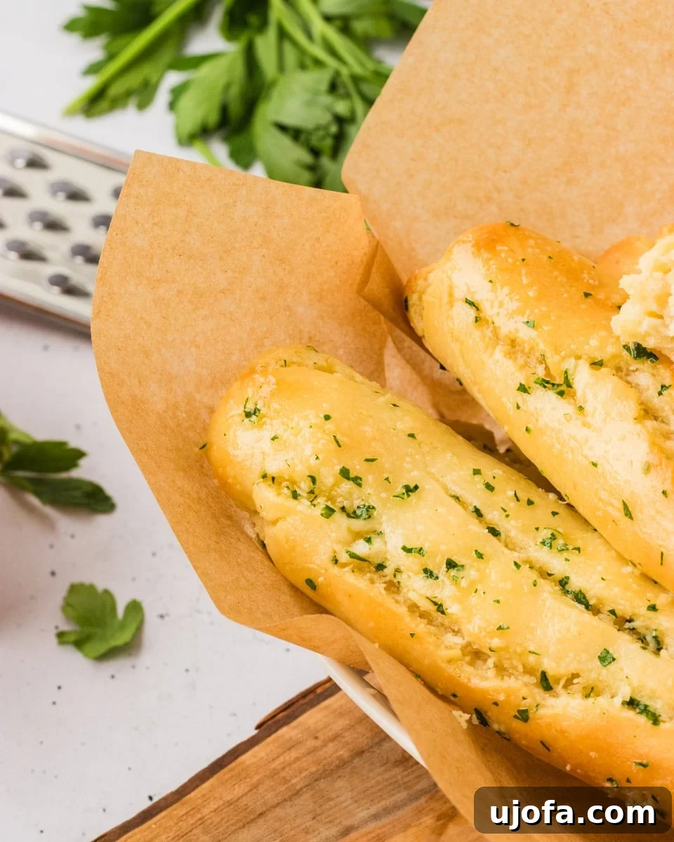 Close-up of golden gluten-free breadsticks topped with garlic and parsley, served in a parchment-lined bowl, showcasing their crisp, buttery crust and inviting aroma.