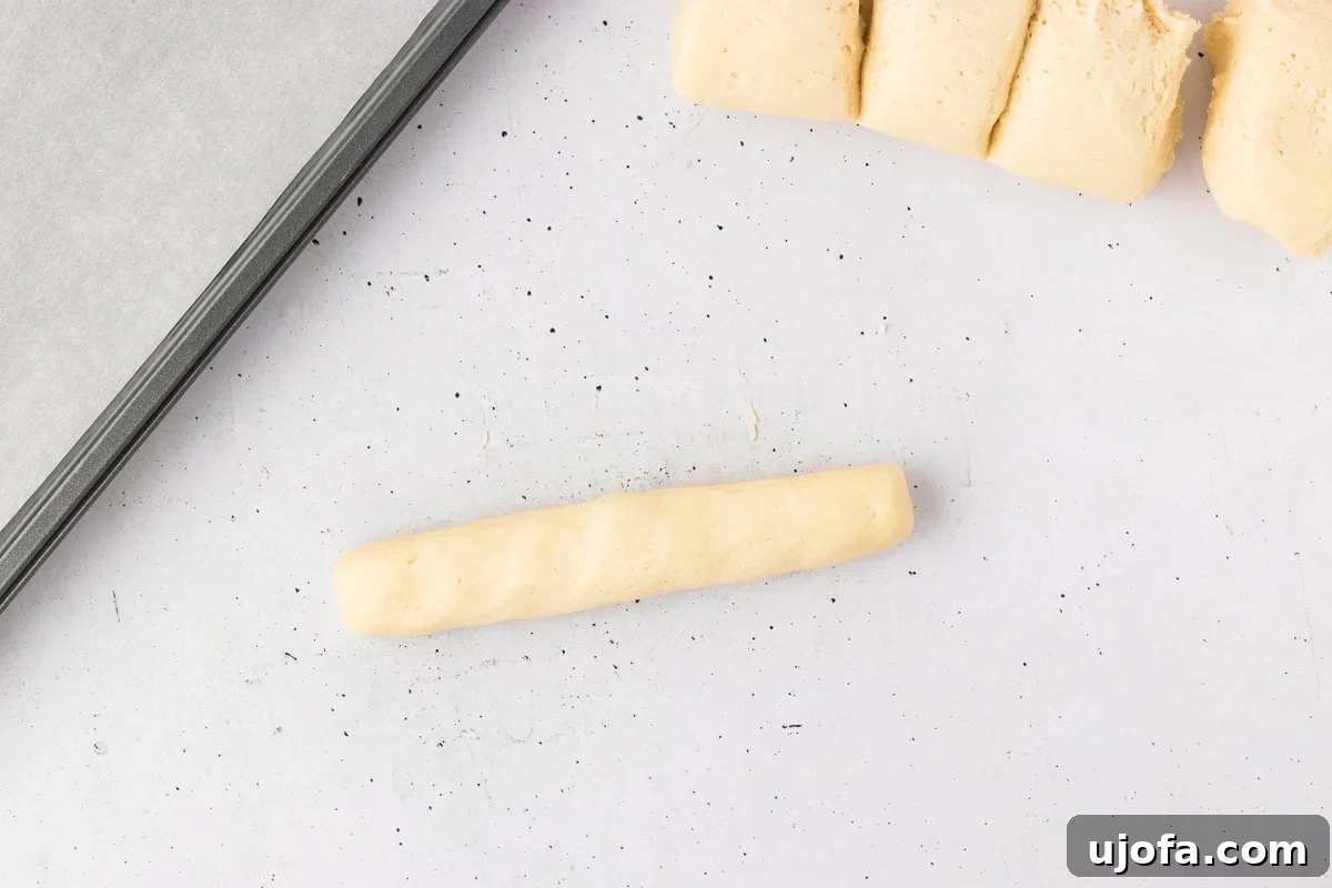 A single portion of gluten-free dough expertly shaped into a short, uniform log, demonstrating the perfect form before baking into a breadstick.