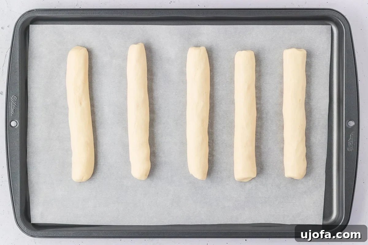 Five perfectly shaped gluten-free breadsticks, evenly spaced and ready for baking, arranged on a parchment-lined baking sheet.