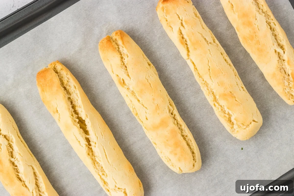 Freshly baked gluten-free breadsticks, golden and lightly crisp on top, cooling on a parchment-lined baking sheet, exuding a warm aroma.