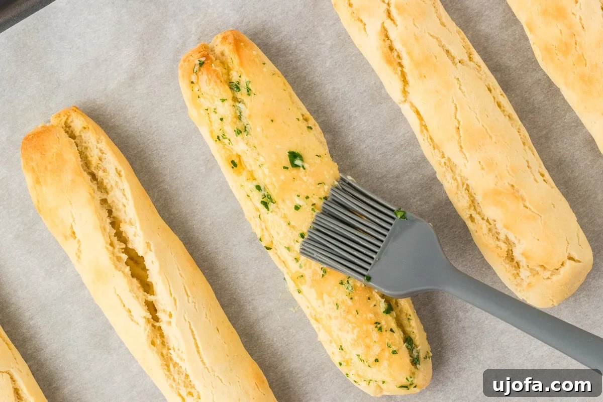 A silicone brush gracefully applying a generous layer of fragrant garlic herb butter onto warm, freshly baked gluten-free breadsticks, enhancing their golden appeal.