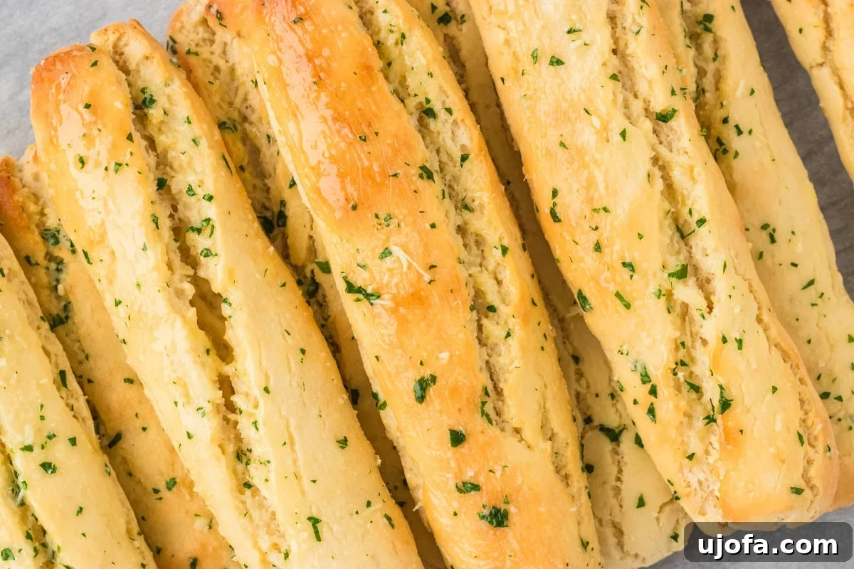 A close-up shot of several golden gluten-free breadsticks, beautifully brushed with garlic butter and garnished with fresh parsley, ready to be enjoyed.