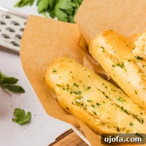 Close-up of golden gluten-free breadsticks topped with garlic and parsley, served in a parchment-lined bowl, highlighting their perfect golden hue.