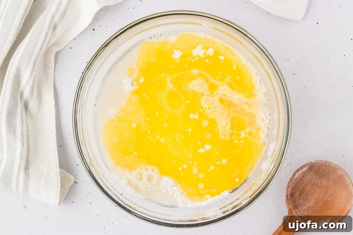 Bowl of wet ingredients, including melted butter, room temperature beaten eggs, and warm water, being added to the dry flour mixture for gluten-free breadstick dough.