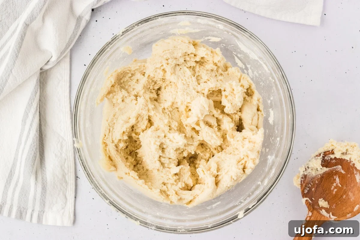 Gluten-free breadstick dough, mixed into a thick, slightly sticky batter, resting in a clear glass bowl, ready for manual kneading.