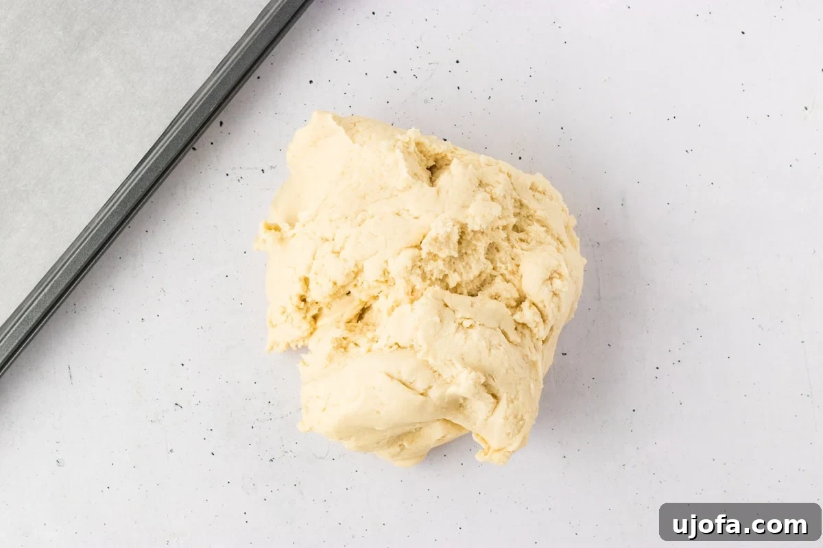 A portion of gluten-free breadstick dough, perfectly mixed, placed on a lightly floured surface next to a parchment-lined baking tray, ready for shaping.