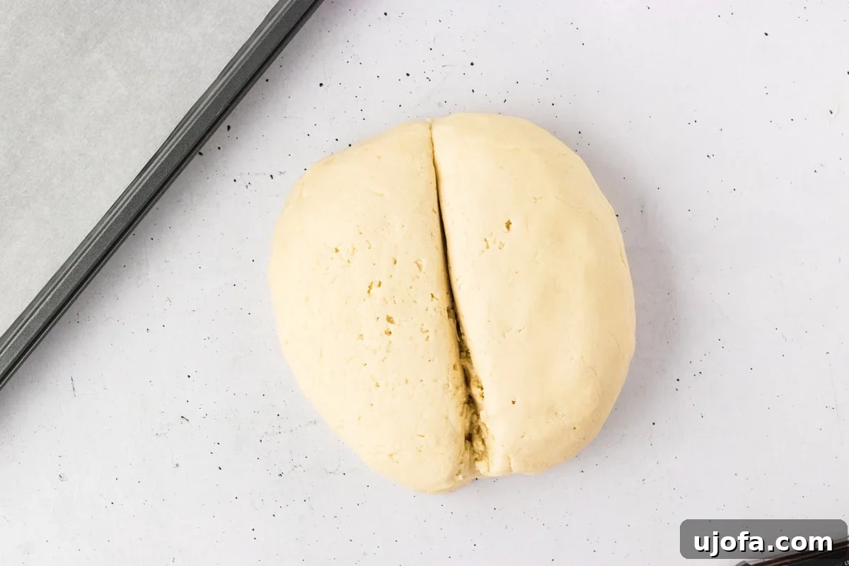 Gluten-free dough ball expertly split in half, demonstrating even division, ready to be further portioned for individual breadsticks.