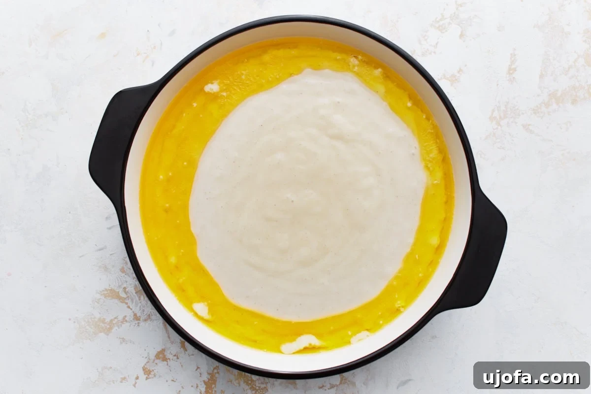 The smooth cobbler batter has been poured into the center of the baking dish, gracefully resting on the melted butter with the liquid butter surrounding it.