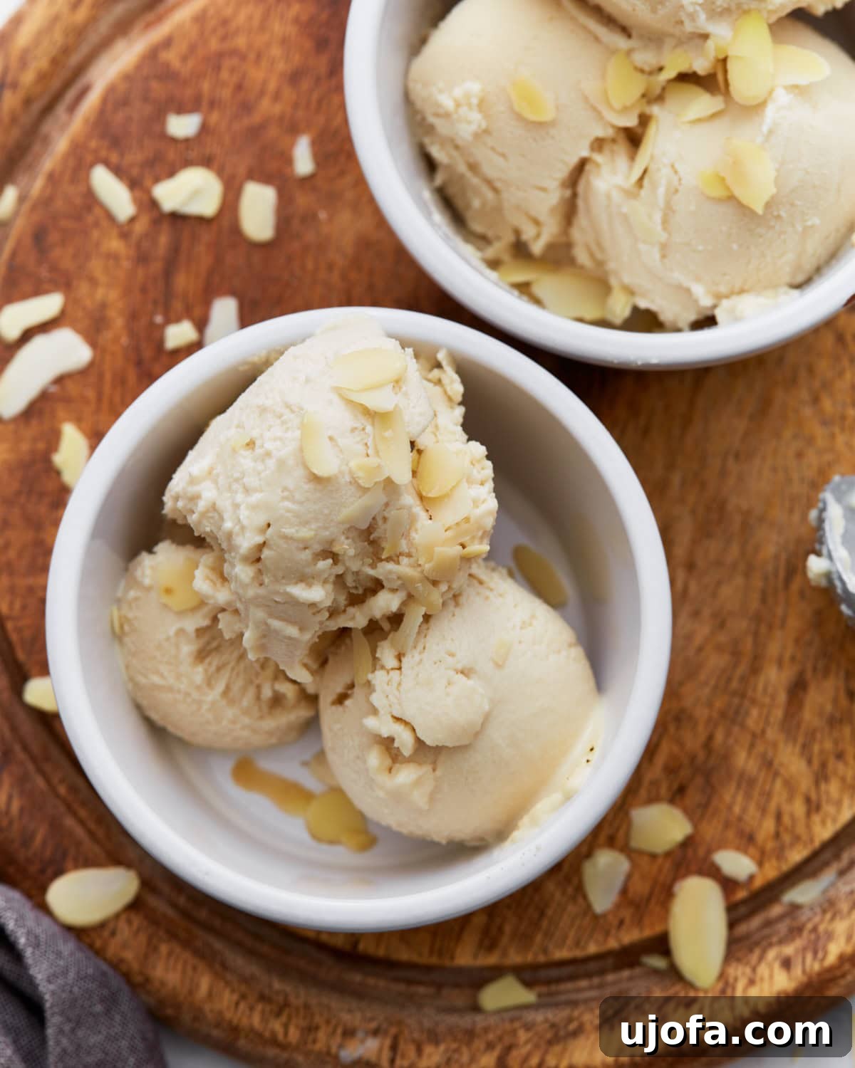 Creamy Almond Dream 2 Close-up of creamy almond milk ice cream scooped into a white ramekin, topped with sliced almonds, sitting on a wooden board.
